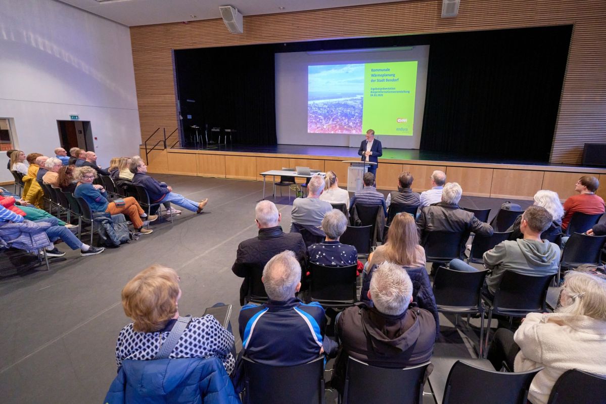 Im Saal der Bendorfer Stadthalle sitzen zahlreiche Besucherinnen und Besucher in mehreren Reihen und folgen einem Vortrag zur kommunalen Wärmeplanung. Auf der Bühne vor ihnen präsentiert eine Person die Inhalte, während im Hintergrund eine große Leinwand mit der zugehörigen Präsentationsfolie sichtbar ist.