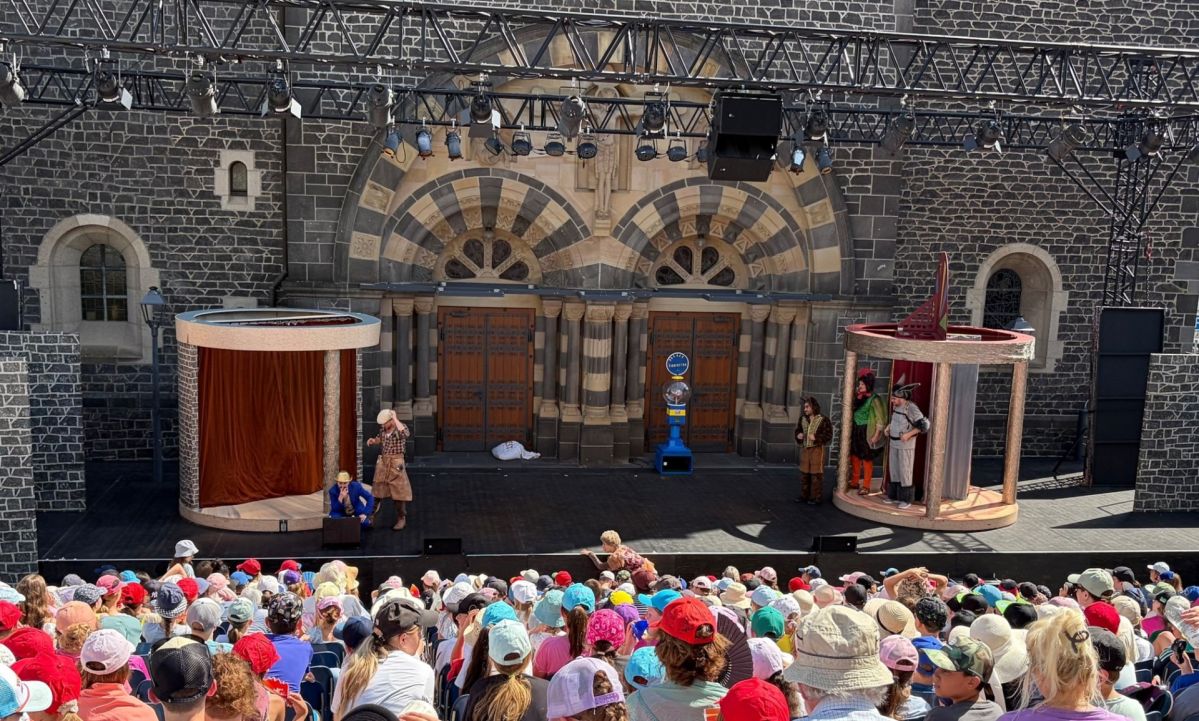 Burgfestspiele Mayen Hunderte Kinder verfolgen bei den Burgfestspielen Mayen die Aufführung des Märchens „Die Bremer Stadtmusikanten“ auf einer Bühne vor der Herz‑Jesu‑Kirche. Auf der Bühne sind mehrere Darstellende sowie die Kulissen des Familienstücks zu sehen.