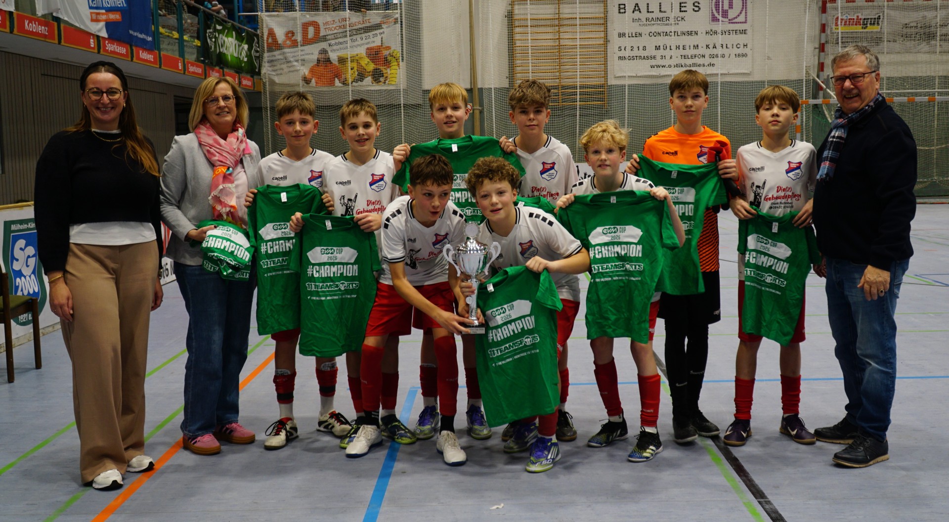 Die Gewinnermannschaft der Sportfreunde Eisbachtal posiert in der Sporthalle mit ihrem Pokal und grünen Champion‑T‑Shirts, gemeinsam mit drei Personen, die den Preis überreichten.
