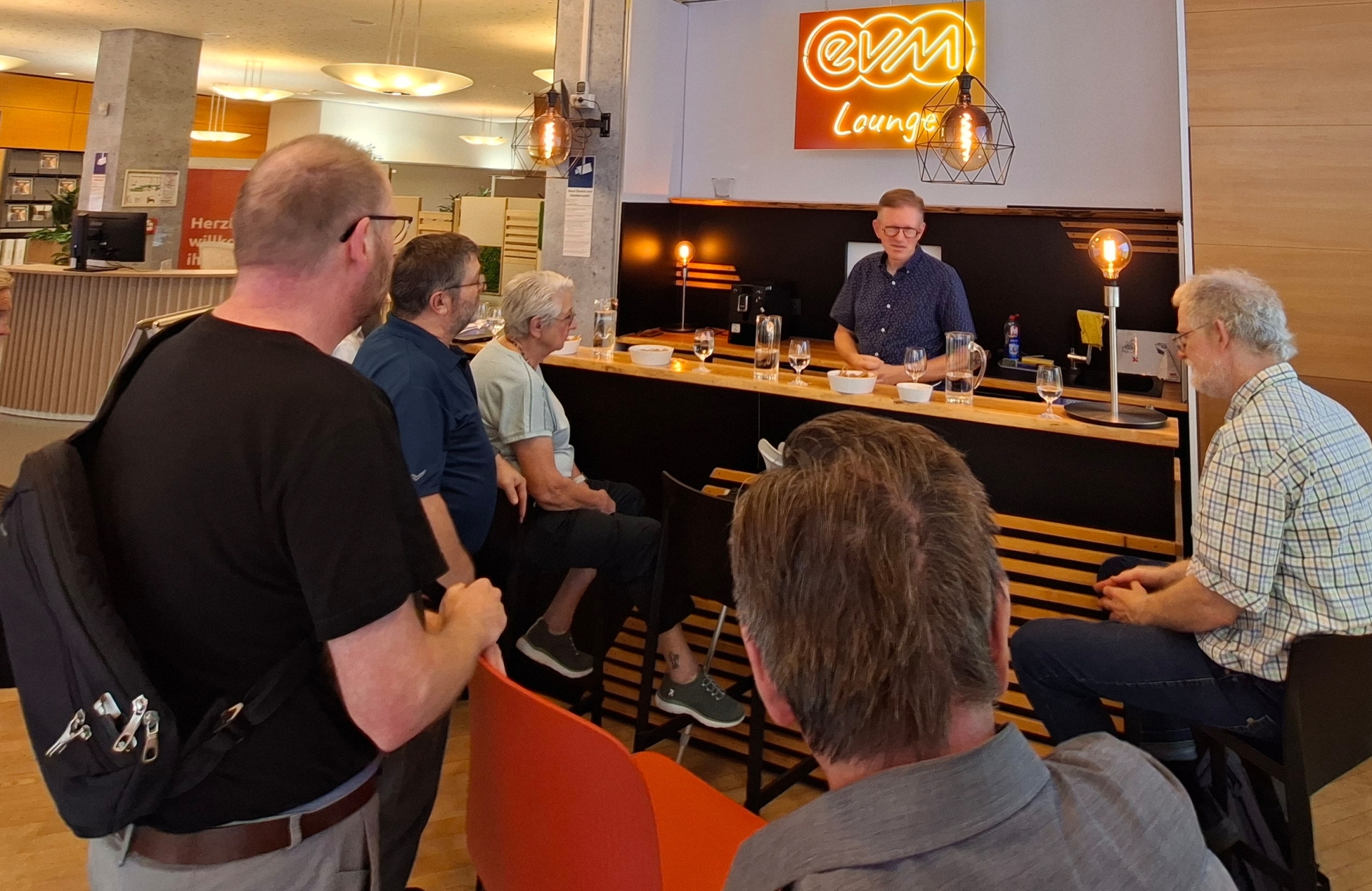 Mehrere Besucherinnen und Besucher sitzen und stehen in der evm‑Lounge im Kundenzentrum der Energieversorgung Mittelrhein (evm) in Koblenz. Marcelo Peerenboom, Leiter der Stabsstelle Kommunikation der evm, beantwortet im Rahmen des ersten „Energietreffs“ Fragen rund um Energiewende, Smart Meter, Gasnetze und die zukünftige Energieversorgung.