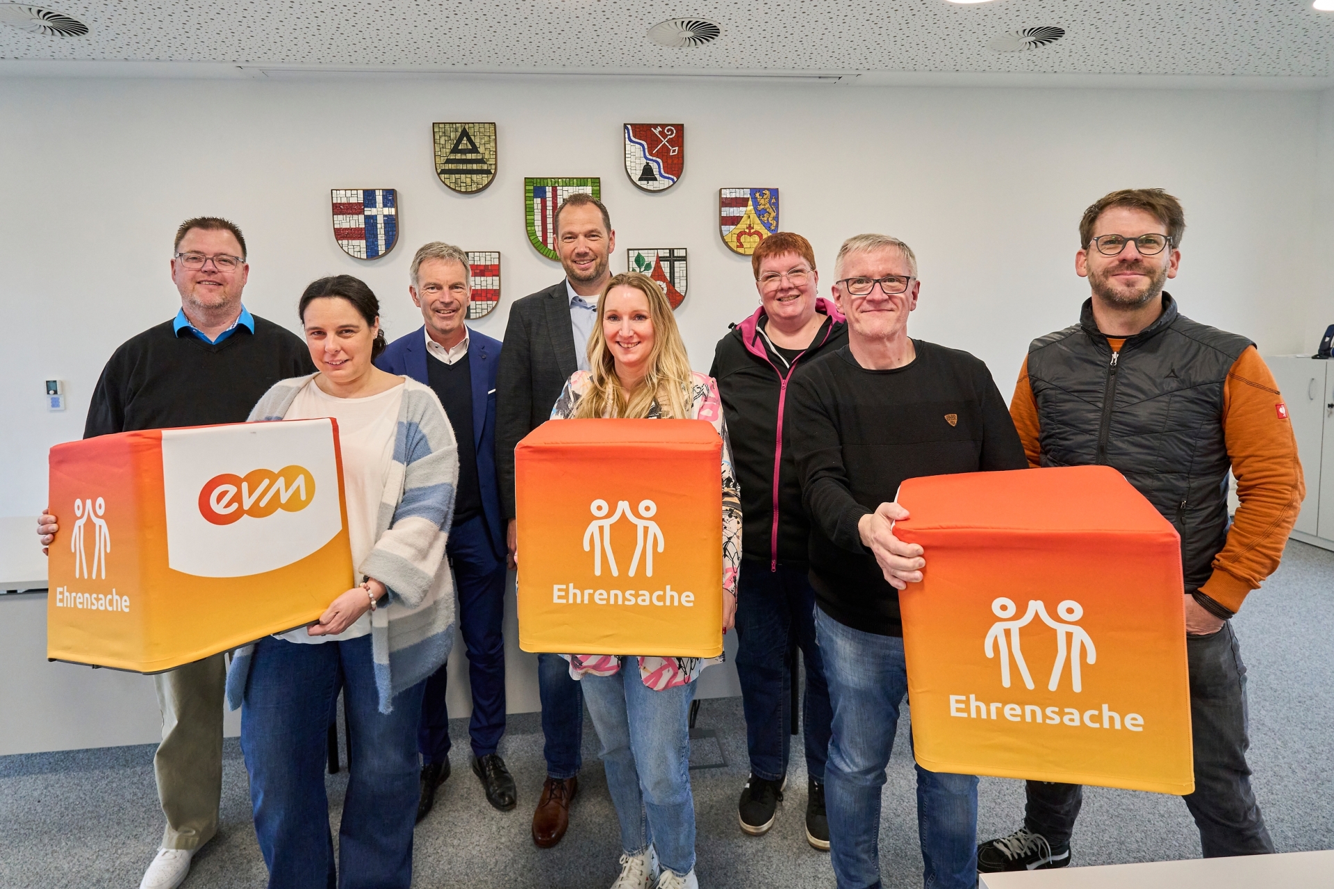 Vertreterinnen und Vertreter von vier Schul‑Fördervereinen stehen gemeinsam mit Norbert Rausch von der evm und Bürgermeister Manuel Seiler im Sitzungssaal der Verbandsgemeinde Dierdorf und halten Spendenboxen des Programms „evm‑Ehrensache“ zur symbolischen Übergabe von insgesamt 2.000 Euro.