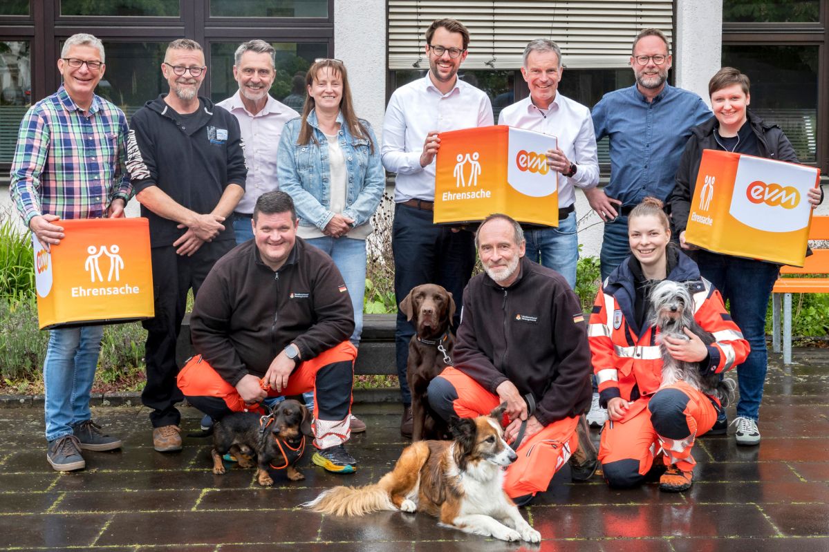 Norbert Rausch und Hubertus Hacke‑Dietze von der evm sowie Verbandsbürgermeister Sven Schür stehen mit Vertreterinnen und Vertretern mehrerer Vereine, darunter eine Rettungshundestaffel mit Hunden, bei der Übergabe der „evm‑Ehrensache“-Spende vor einem Gebäude.