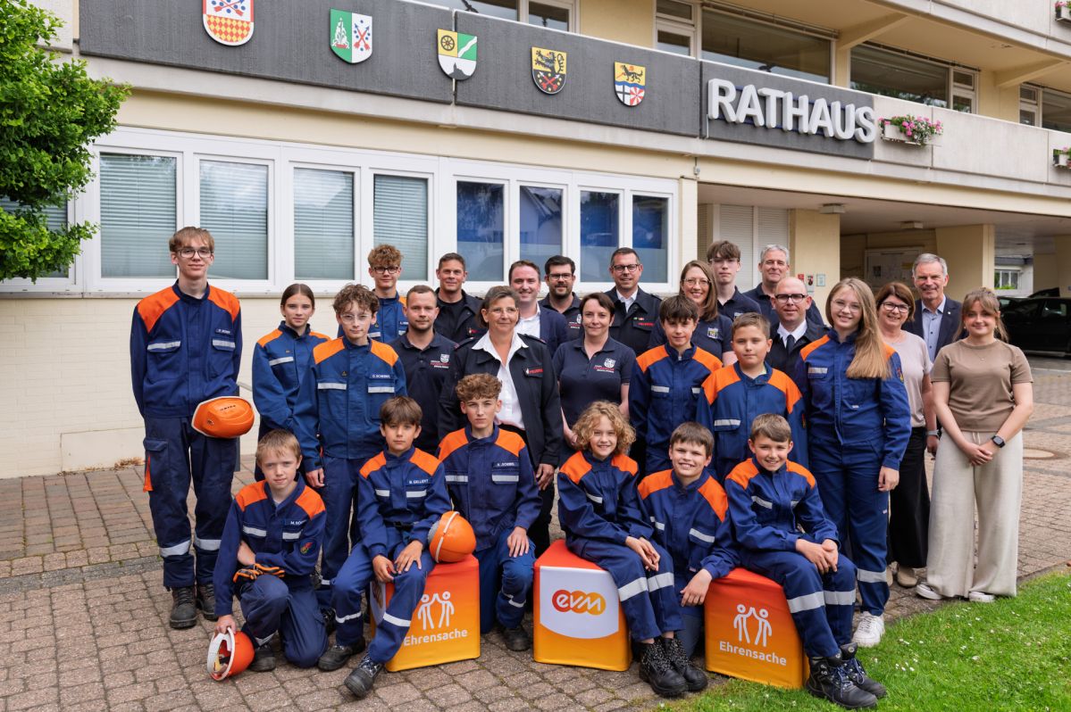 Norbert Rausch (evm) und Bürgermeister Marcel Caspers stehen mit Mitgliedern der Jugend‑ und Bambinifeuerwehren der Verbandsgemeinde Bad Breisig vor dem Rathaus bei der Übergabe der „evm‑Ehrensache“-Spende.