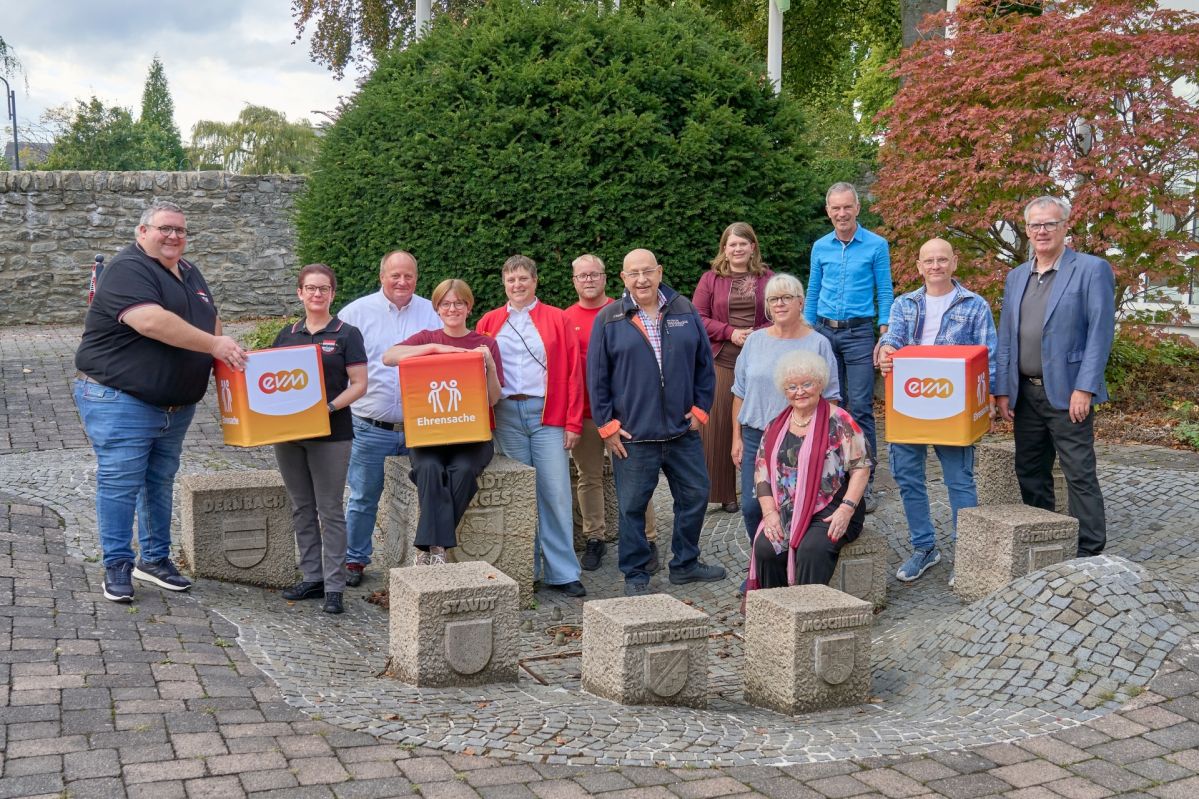 evm-Ehrensache VG Wirges Vertreterinnen und Vertreter des Kulturkreis Mogendorf e.V., der Kirmes Altstars Dernbach e.V. und der DLRG Ortsgruppe Wirges e.V. stehen gemeinsam mit Norbert Rausch von der evm und Bürgermeisterin Alexandra Marzi auf einem Platz im Freien. Mehrere Personen halten „evm‑Ehrensache“-Spendenboxen, die symbolisch für die Förderung der Vereine aus dem Spendenprogramm stehen.
