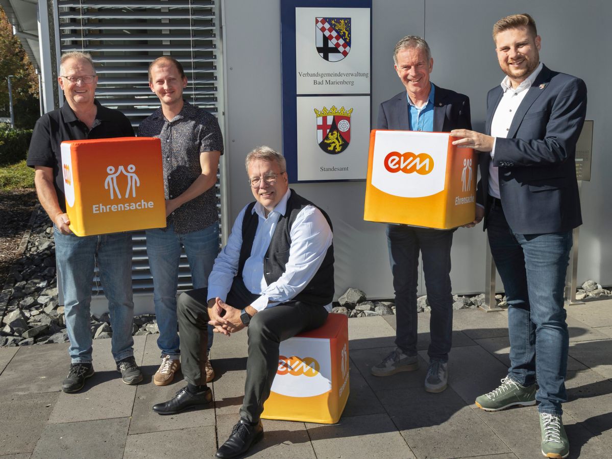 evm-Ehrensache VG Bad Marienberg Fünf Personen stehen vor dem Gebäude der Verbandsgemeinde Bad Marienberg und halten „evm‑Ehrensache“-Spendenboxen. Zu sehen sind Norbert Rausch von der evm, Bürgermeister Marvin Kraus sowie Vertreter des Ski‑Club Bad Marienberg Unnau e.V. und des Ski‑Club Kirburg e.V.. Die Aufnahme entstand bei der symbolischen Übergabe der Spenden aus dem Programm „evm‑Ehrensache“.