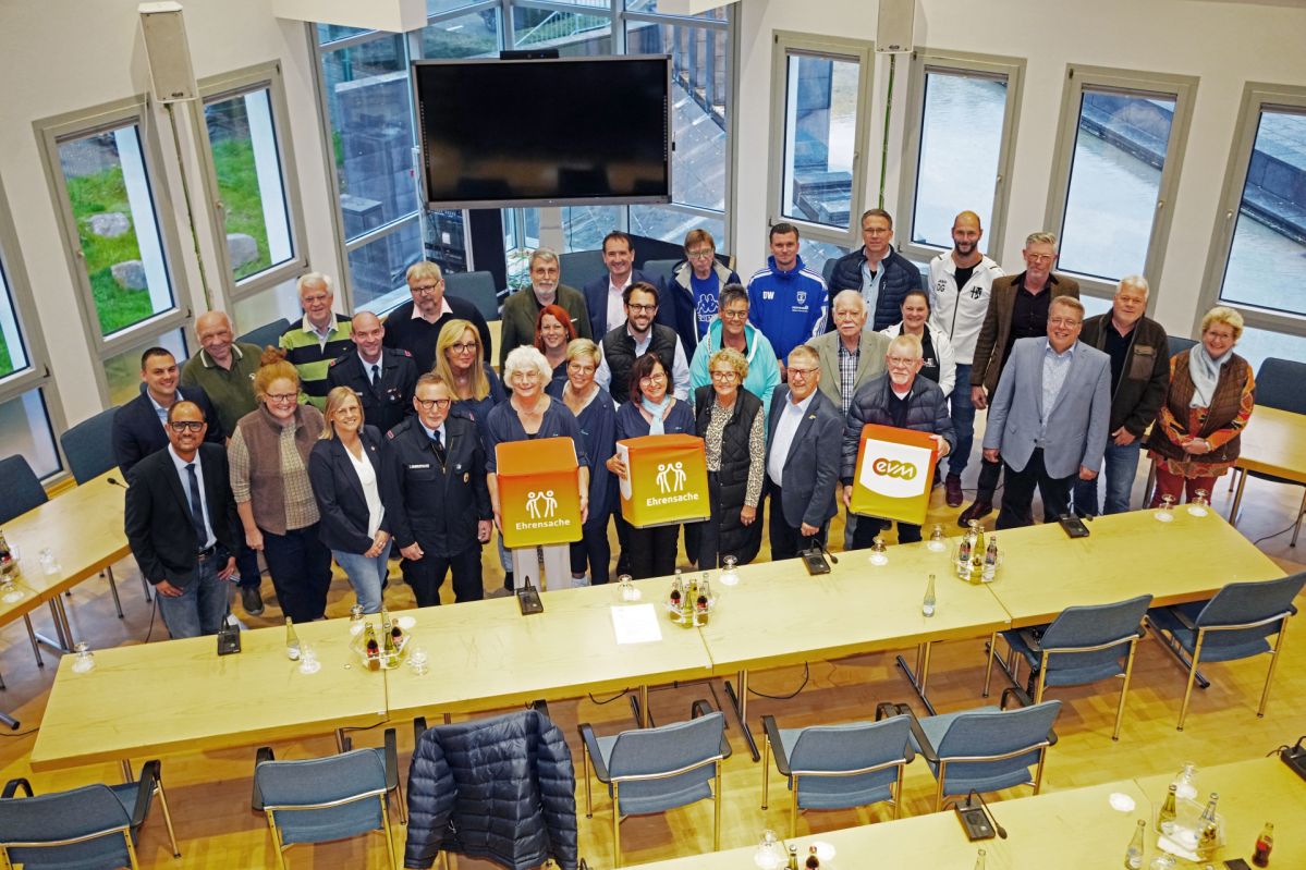 Eine Gruppe von Menschen stehen in einem Saal und lächeln freundlich. Sie halten orangene Würfel mit der Aufschrift "evm Ehrensache".