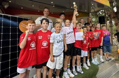 Eine Jugendmannschaft des HV Vallendar steht auf einer Bühne vor dem evm‑Infomobil. Die Spielerinnen und Spieler präsentieren einen Pokal und eine Urkunde für den ersten Platz beim evm‑Cup. Im Hintergrund stehen Betreuende sowie die Moderation der Siegerehrung.
