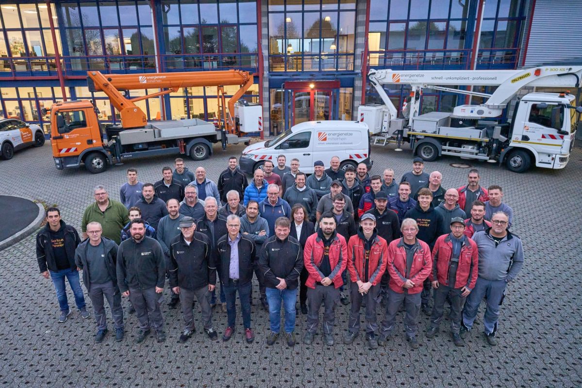 Mitarbeitende der Energienetze Mittelrhein stehen vor dem Betriebsgebäude des Standorts Hahn am See für ein Gruppenfoto. Im Hintergrund sind mehrere Servicefahrzeuge und Hubarbeitsbühnen des Netzbetreibers zu sehen. Das Team betreut von hier aus die Strom- und Gasversorgung in großen Teilen des Westerwalds und unterstützt die Umsetzung der Energiewende in der Region.