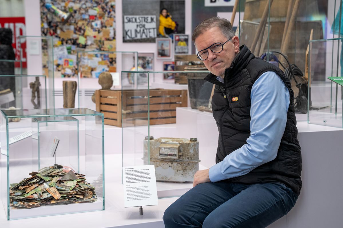 Marcelo Peerenboom von der evm sitzt in der Dauerausstellung im Haus der Geschichte in Bonn neben dem Gaszähler aus dem Ahrtal, der an die Flutkatastrophe 2021 erinnert.