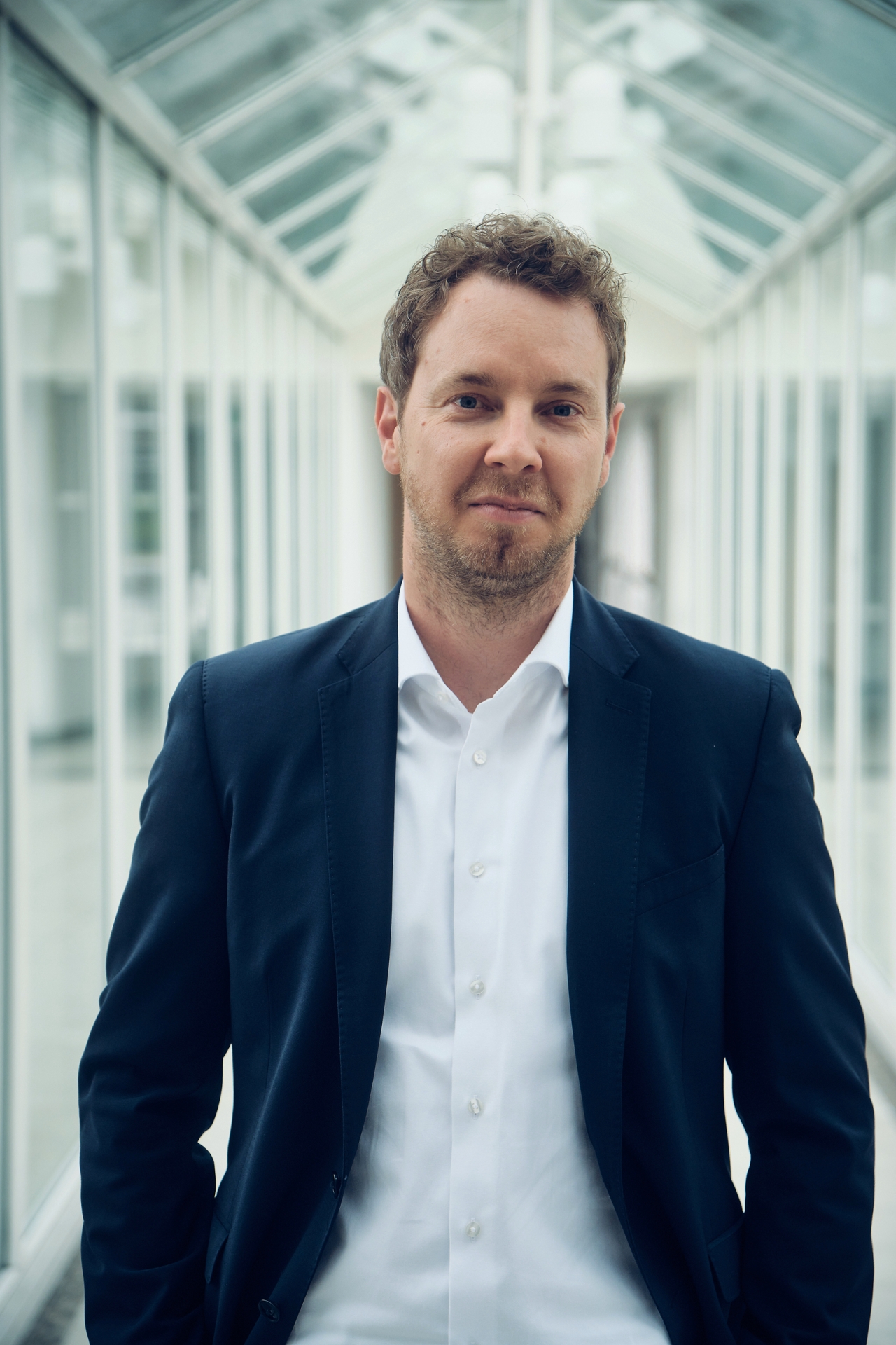 Christoph Hesse Christoph Hesse steht in einem verglasten Verbindungsgang eines modernen Bürogebäudes und blickt in die Kamera. Das Vorstandsmitglied der evm trägt ein dunkles Sakko mit weißem Hemd. Anlass des Porträts ist die Verlängerung seines Vertrags als Mitglied des Vorstands um weitere fünf Jahre.