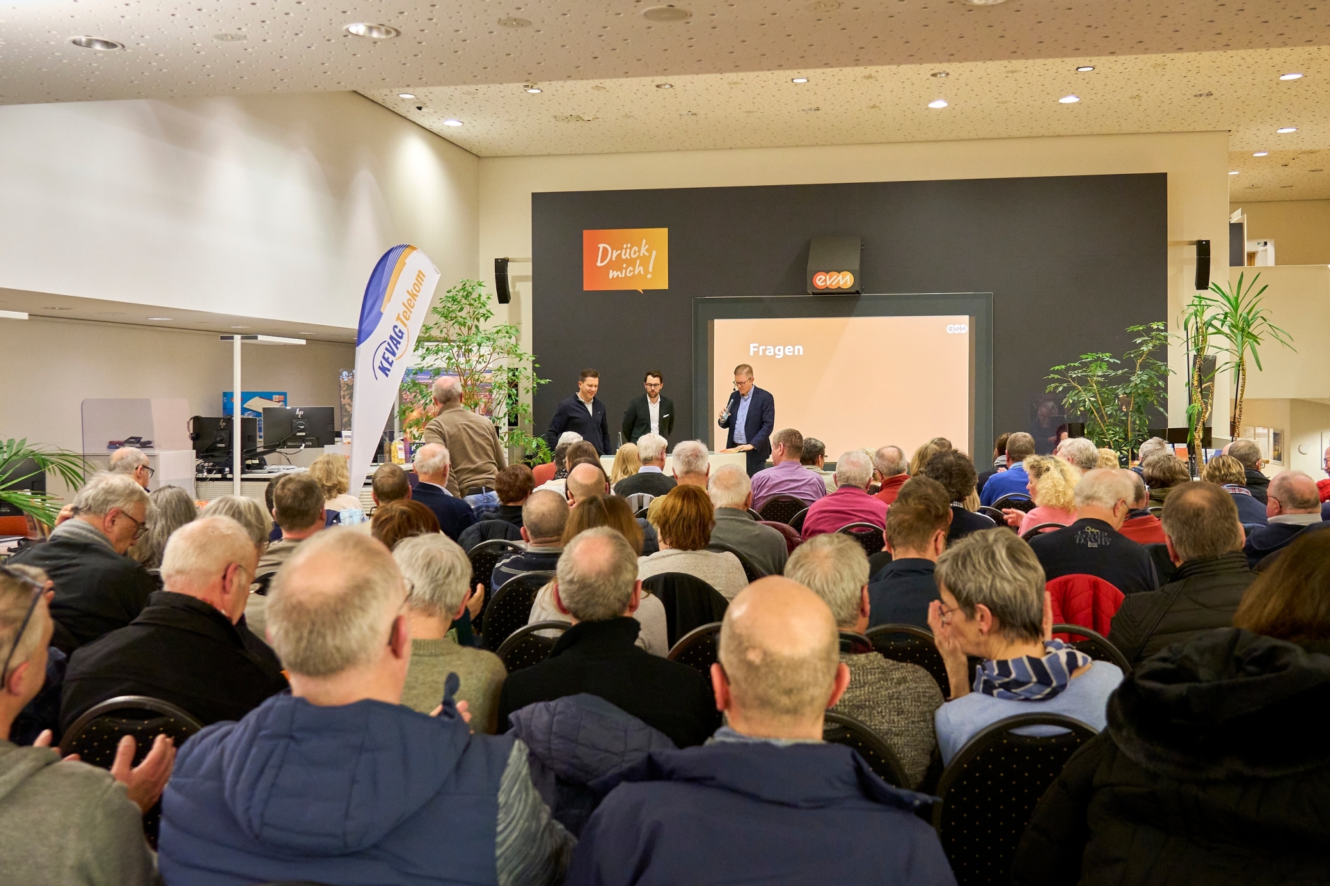 Publikumsveranstaltung im evm‑Kundenzentrum Koblenz: Viele Teilnehmende sitzen in Reihen und verfolgen eine Präsentation zu Solarenergie, Wärmepumpen und smarter Energiesteuerung, während drei Vortragende vorne auf der Bühne stehen.