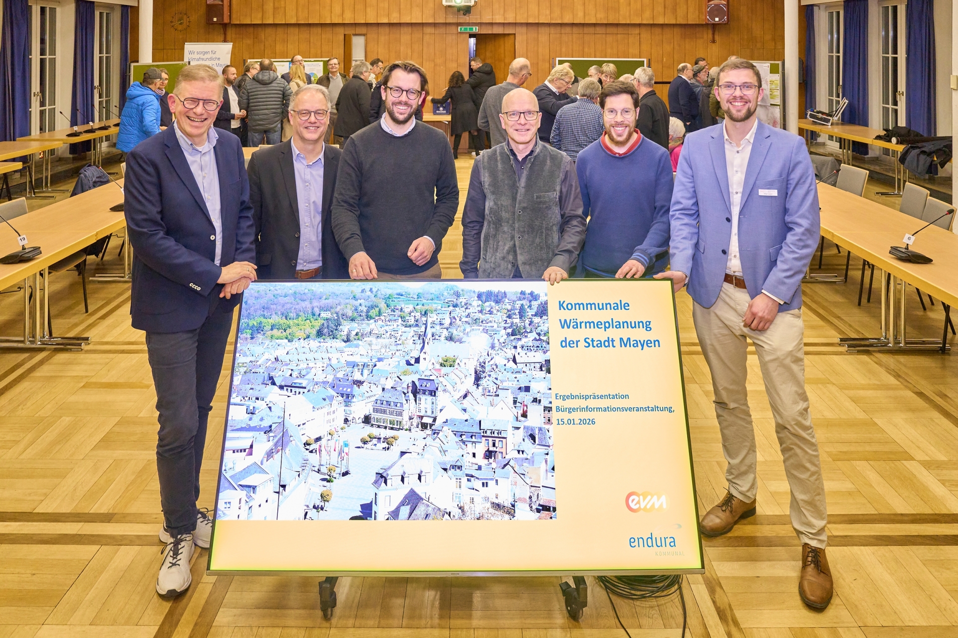 Referenten der Infoveranstaltung zur kommunalen Wärmeplanung der Stadt Mayen stehen vor einer Präsentationstafel im Veranstaltungsraum.