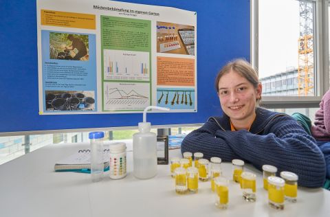 Jugend forscht 2026 - Regionalwettbewerb Koblenz Am „Jugend forscht“-Stand von Ronja Kröger sind Probengefäße mit gelben Flüssigkeiten und Laborutensilien ausgestellt; im Hintergrund hängt ein Poster zum Projekt „Mückenbekämpfung im eigenen Garten“ mit Diagrammen und Versuchsergebnissen.