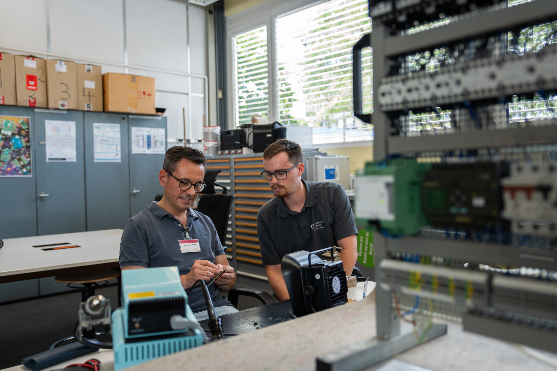 David Langner sitzt gemeinsam mit einem Mitarbeiter der Energienetze Mittelrhein in der Ausbildungswerkstatt an einem Arbeitstisch. Vor ihnen befinden sich elektronische Bauteile und eine Übungsanlage für die Elektrotechnik. Während seines Praktikumstags erhielt der Oberbürgermeister Einblicke in die Ausbildung und technische Arbeitsbereiche der evm-Gruppe.