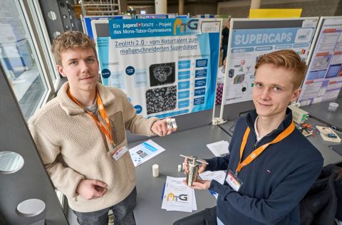 Jugend forscht 2026 - Regionalwettbewerb Koblenz Zwei Teilnehmende präsentieren ihr Projekt „Zeolith 2.0“ am Wettbewerbsstand und halten Proben sowie einen Versuchsbehälter vor einer Stellwand mit Informationen zum Superdünger.