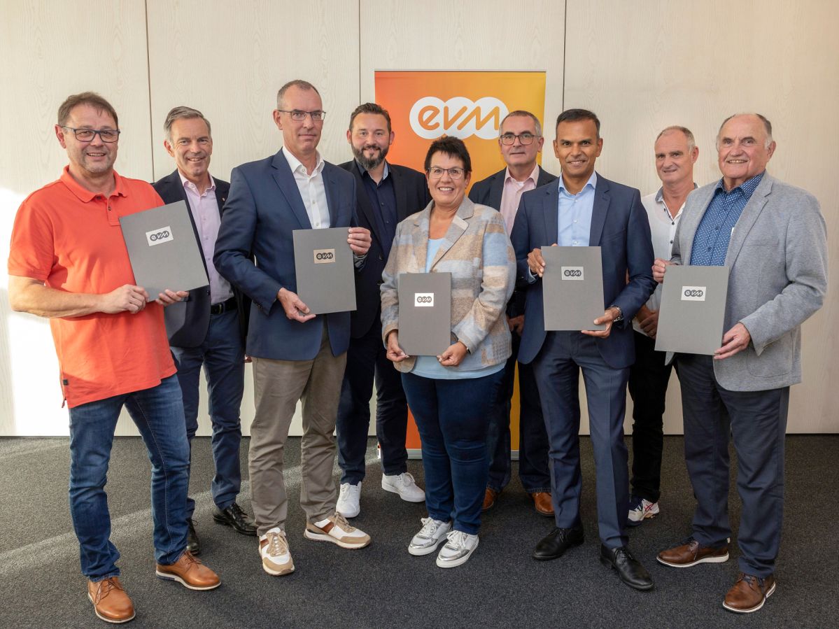 c Röder-Moldenhauer Acht Männer und eine Frau sind professionell gekleidet und lächeln freundlich. Sie halten Graue Mappen mit evm Logo in der Hand.
