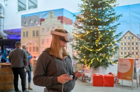 Eine junge Frau in einem grauen Hoodie steht in einem weihnachtlich dekoriertem Raum und trägt eine VR-Brille.