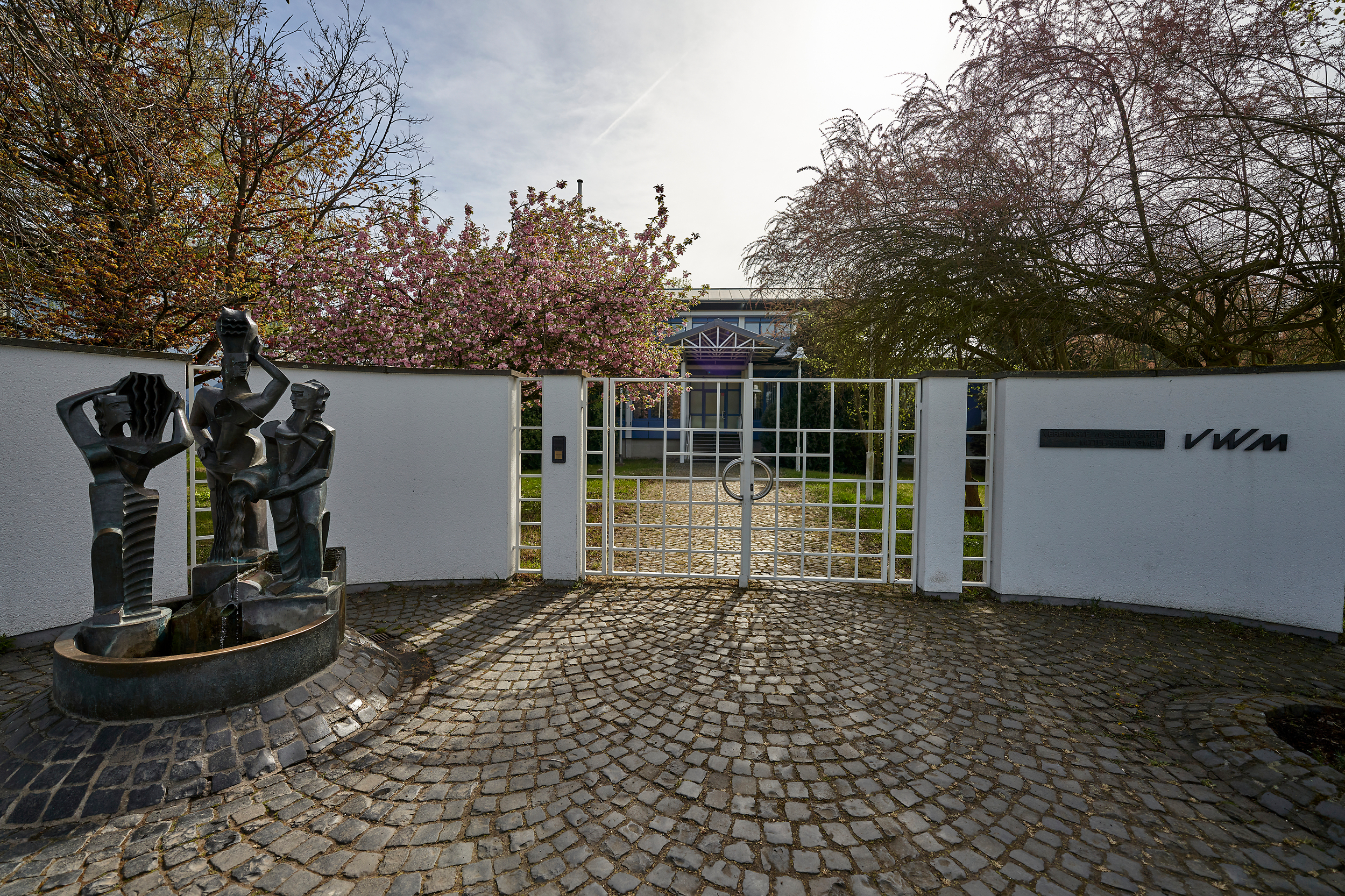 Der Eingang vom Wasserwerk Oberwerth. Eine weiße Wand mit einem Tor, daneben ein kleiner Brunnen.