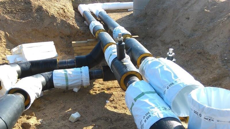 Schwarze Rohre mit weißen Verbindungsstücken  liegen in einem Sandgraben.