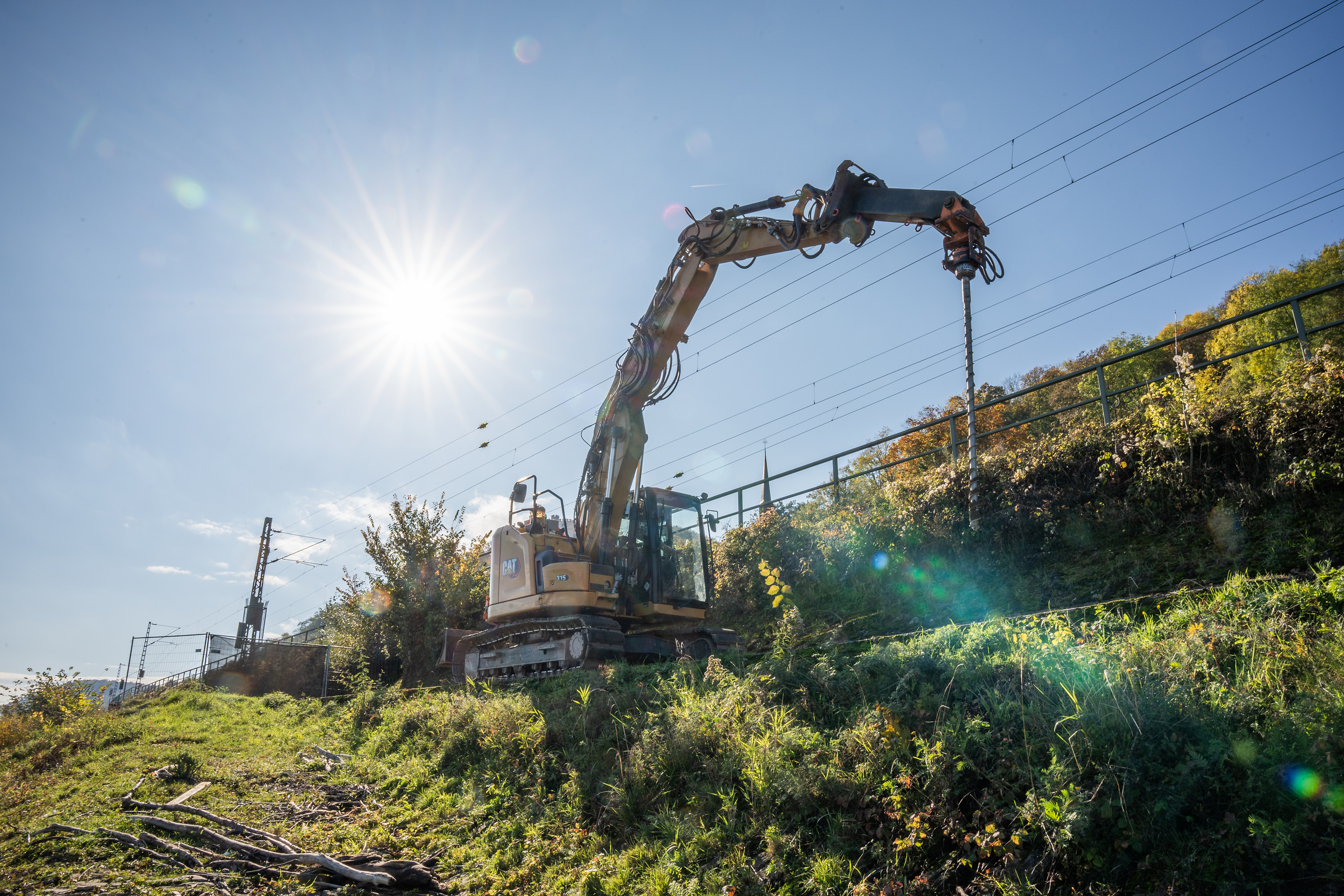 Ein Bagger mit einem Bohrer steht in einer grünen Landschaft mit blauem Himmel