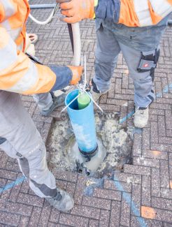Zwei Personen in orangener Schutzkleidung arbeiten an einem Rohr.