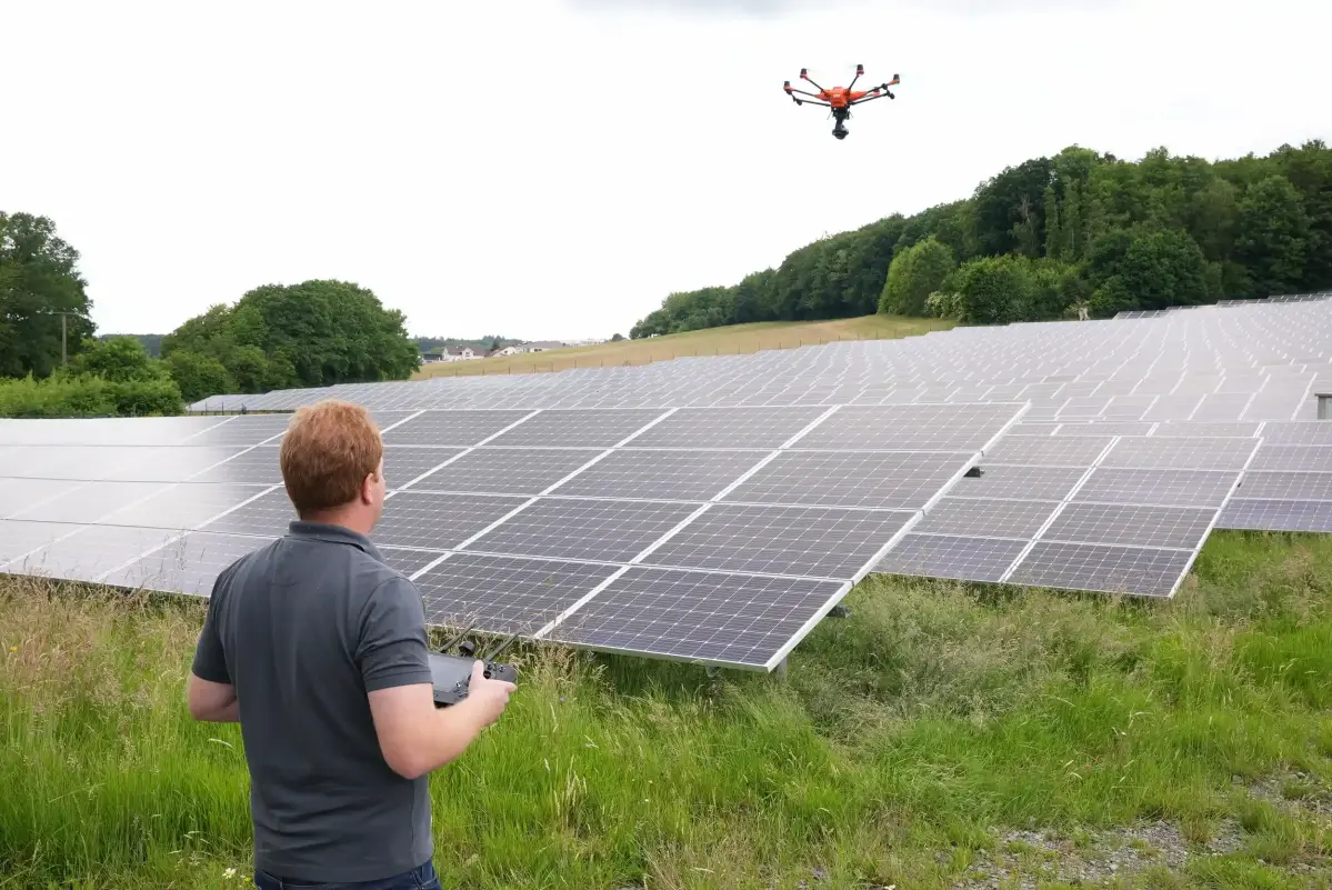 Ein Mann steht vor einem Solarpark und bedient eine Drohne. Er trägt ein graues Poloshirt.