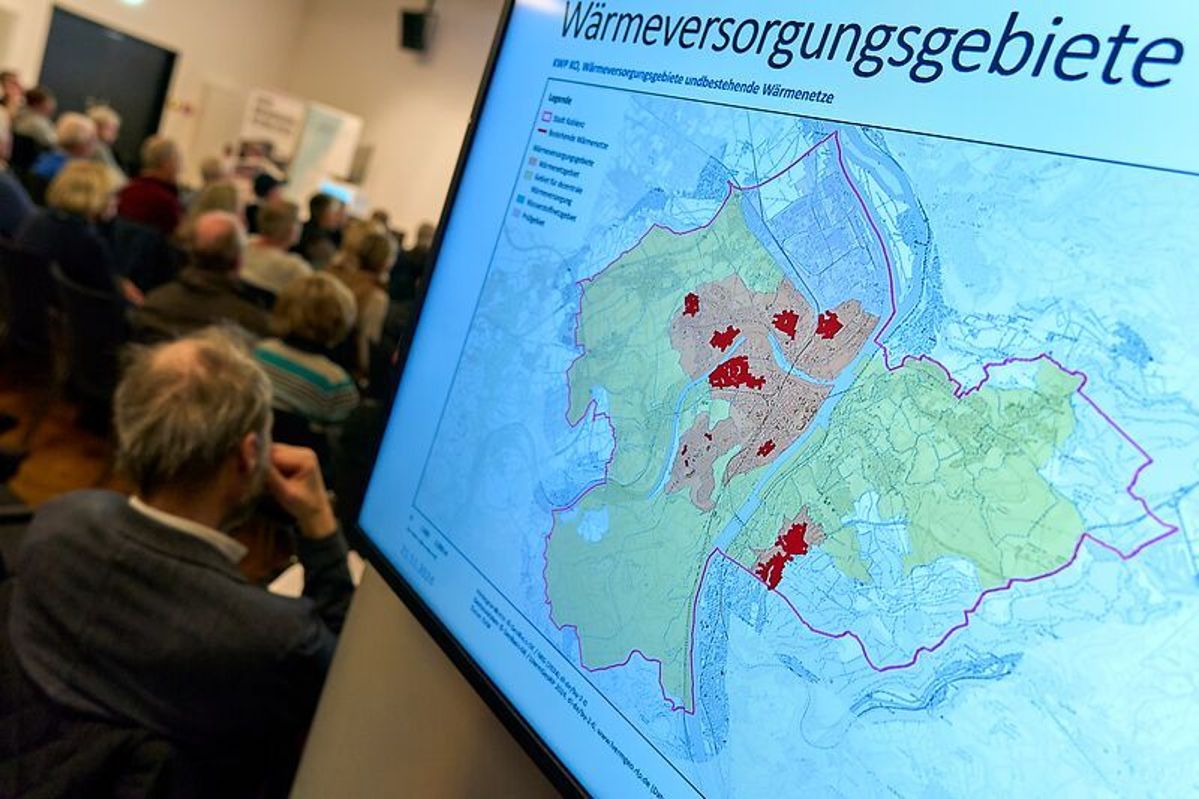 Bürgerinfo Kommunale Wärmeplanung Ein Bildschirm zeigt die Wärmeversorgungsgebiete. Im Hintergrund sind mehrere Menschen in einem Veranstaltungsaal zu erkennen.