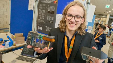 250210SDI1102 Ein Junge hält eine Brille in der Hand und lächelt freundlich.