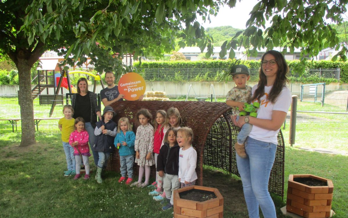 Mehrere Kinder und drei Erwachsene stehen vor einem Tunnel und halten ein Schild mit der Aufschrift "Gemeinsam haben wir die Power".