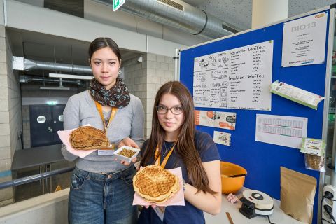 250210SDI1047 Zwei Mädchen halten Waffeln in der Hand und lächeln freundlich.