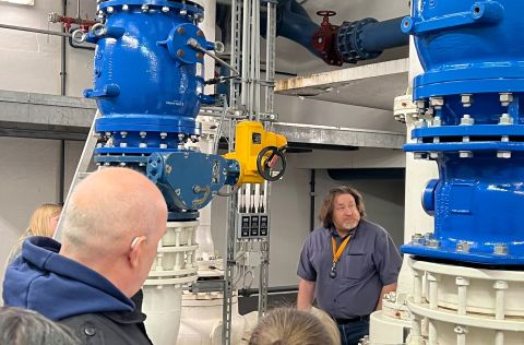 IMG_2331 Mehrere Menschen stehen in einem Raum mit großen blauen Rohren. Ein Mann steht vor ihnen und erklärt etwas.