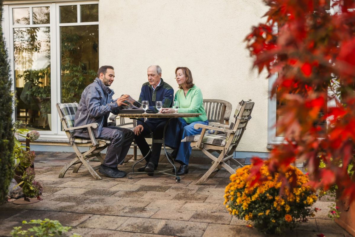 Im Garten sitzen drei Personen um einen Tisch im Verkaufsgesräch