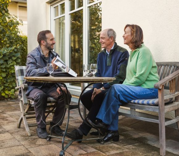 Im Garten sitzen drei Personen um einen Tisch im Verkaufsgesräch Solaranlagen
