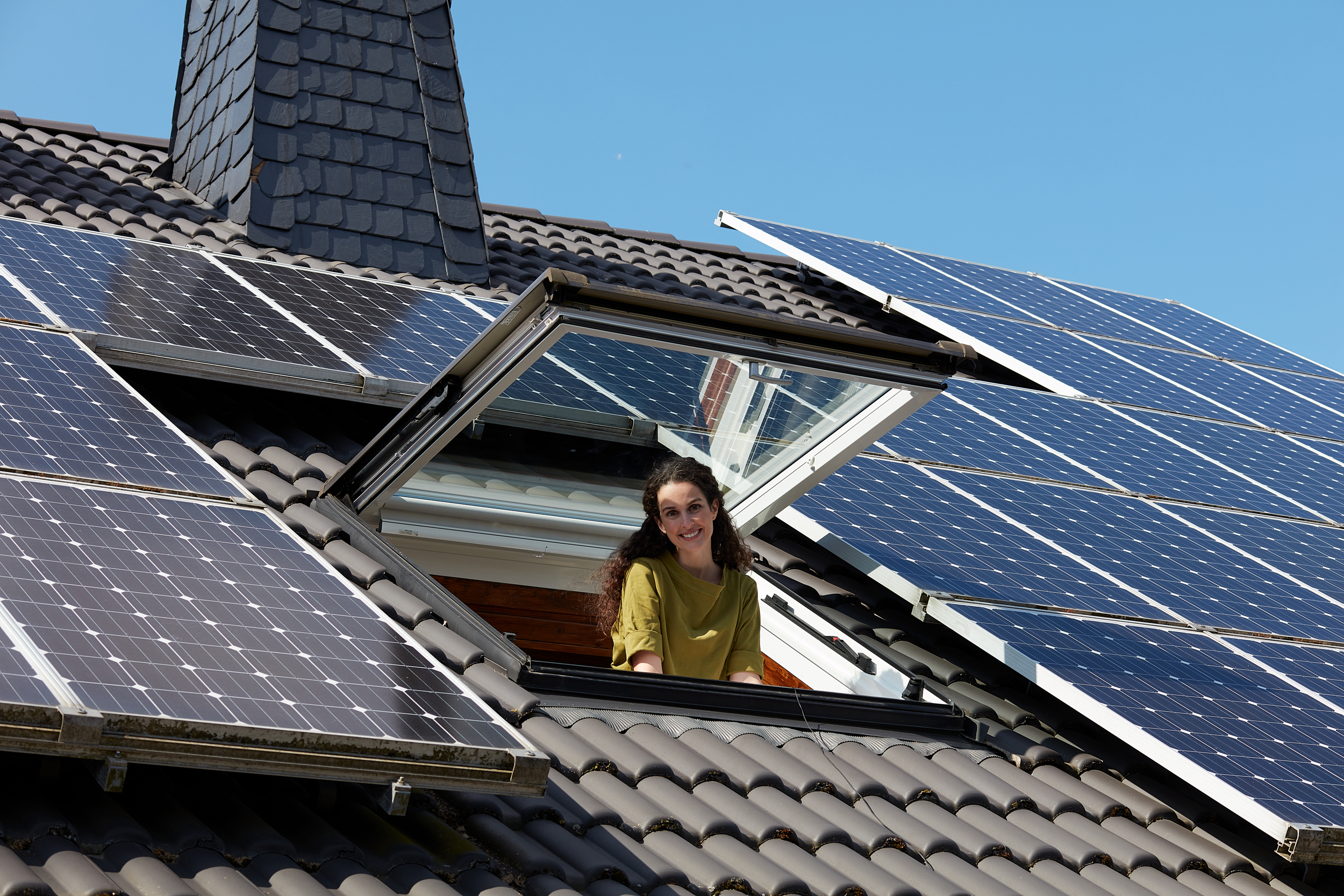 Eine Frau schaut aus einem Dachfenster. Auf dem Dach befinden sich mehrere Solarmodule.