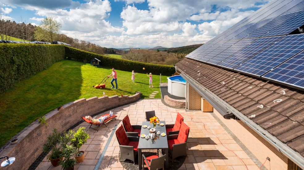 Eine Familie sitzt in einem grünen Garten. Die Luftaufnahme zeigt zudem ein Haus mit einer Solaranlage.