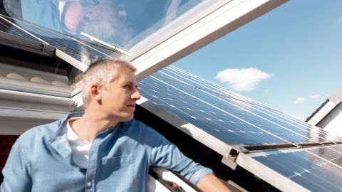 Ein Mann steht in einem Dachfenster und schaut raus. Auf dem Dach befindet sich eine Solaranlage.