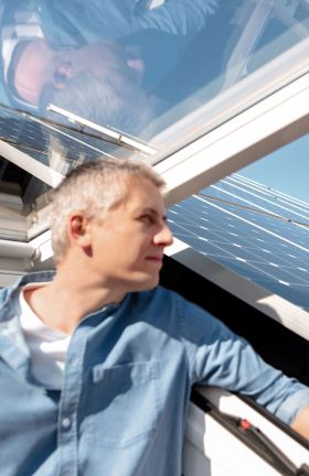 Ein Mann steht in einem Dachfenster und schaut raus. Auf dem Dach befindet sich eine Solaranlage.