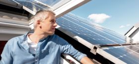 Ein Mann steht in einem Dachfenster und schaut raus. Auf dem Dach befindet sich eine Solaranlage.