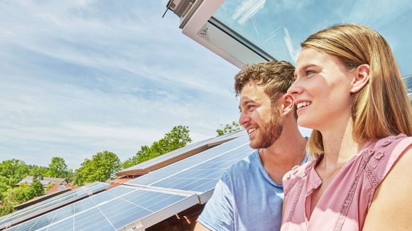 Solaranlage auf Schrägdach Ein Paar steht in einem Dachfenster und schauen raus. Auf dem Dach befindet sich eine Solaranlage.