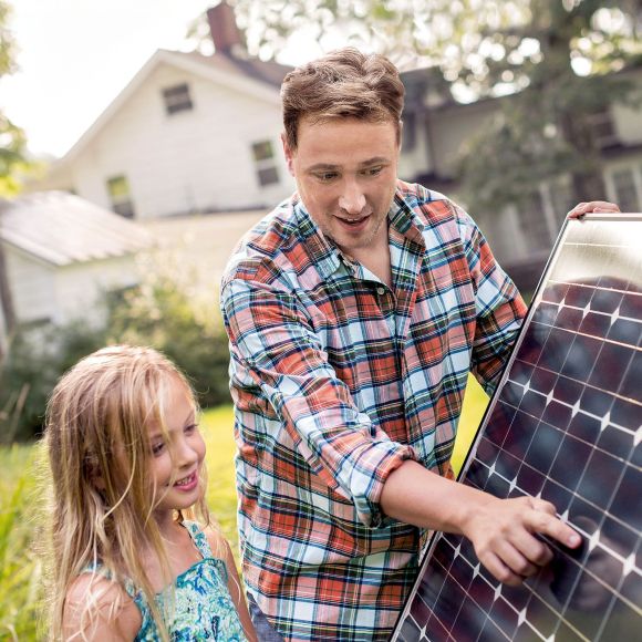 Ein Mann hält ein Solarpanel und erklärt einem Mädchen etwas.