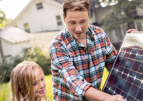 Ein Mann hält ein Solarpanel und erklärt einem Mädchen etwas.
