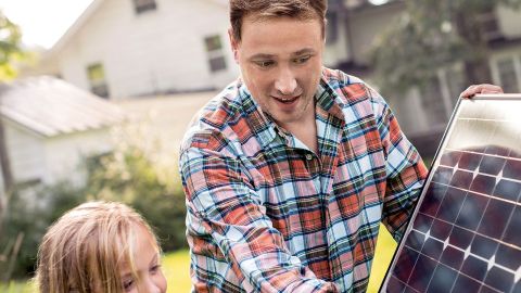 Ein Mann hält ein Solarpanel und erklärt einem Mädchen etwas.