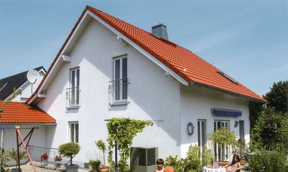Ein junge steht vor einem Haus mit einer Wärmepumpe und hält einen Ball.