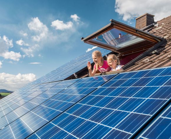 Kinder schauen aus einem Dachfenster auf die Solaranlage.