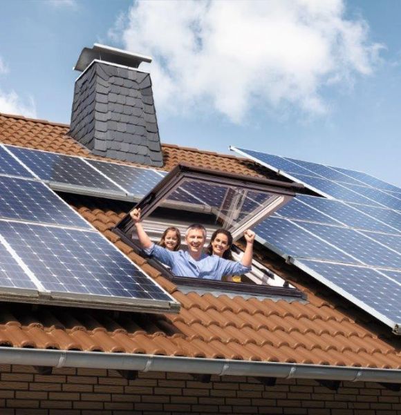 Eine Familie steht in einem Dachfenster und schaut fröhlich raus. Auf dem Dach befindet sich eine Solaranlage.