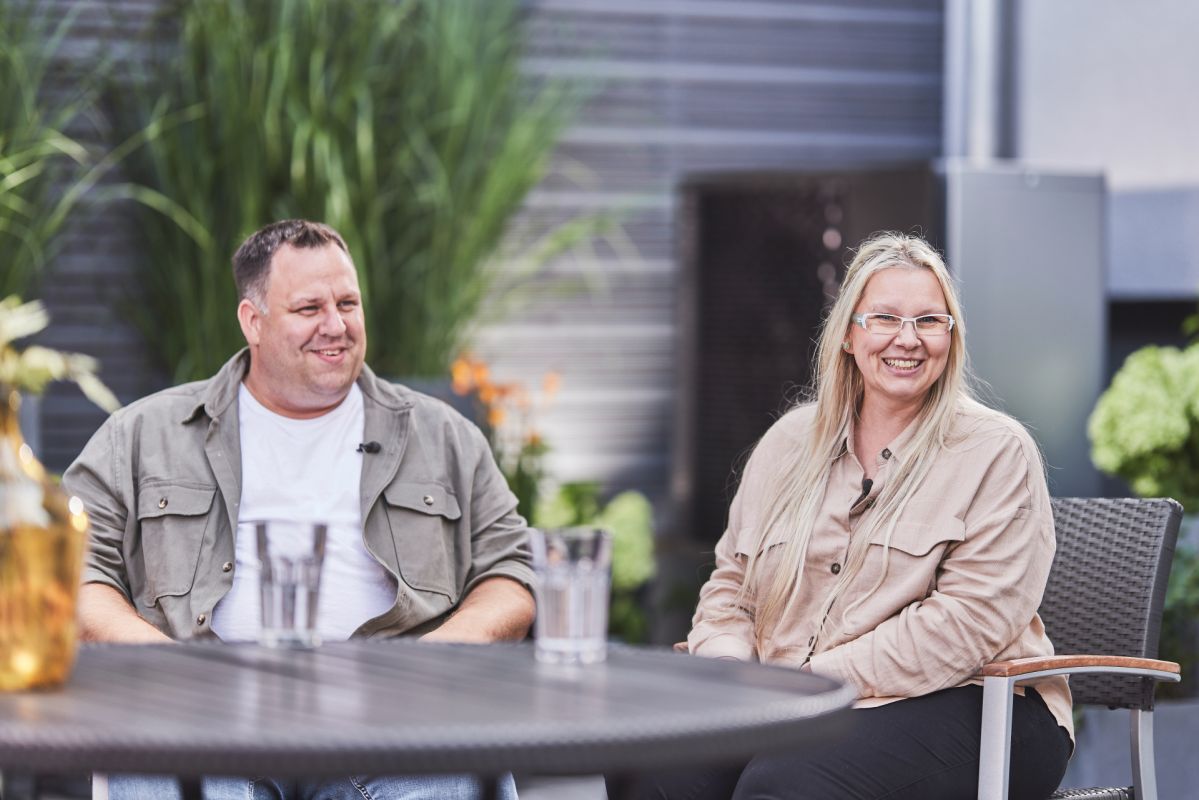 Ein Mann und eine Frau sitzen an einem Tisch draußen und lächeln