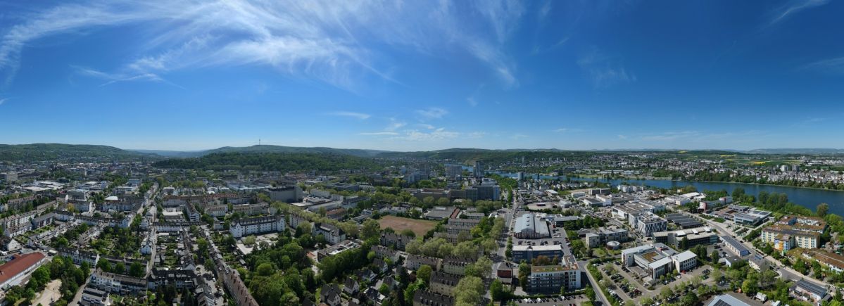 Panoramablick über ein gemischt genutztes Stadtgebiet in Koblenz mit Wohnhäusern, Bürogebäuden, Gewerbeflächen und dem Rhein im Hintergrund.