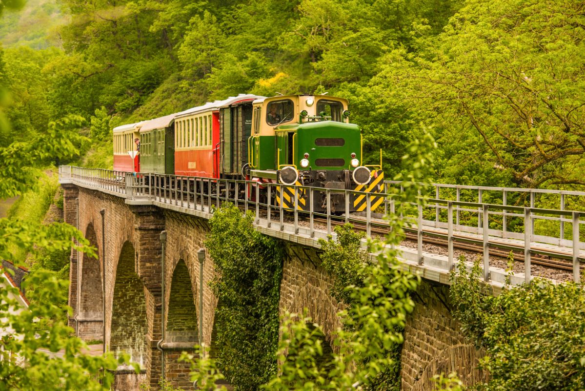 Historischer Zug der Brohltalbahn fährt über ein steinernes Viadukt durch die grüne Landschaft des Brohltals bei Brohl-Lützing.