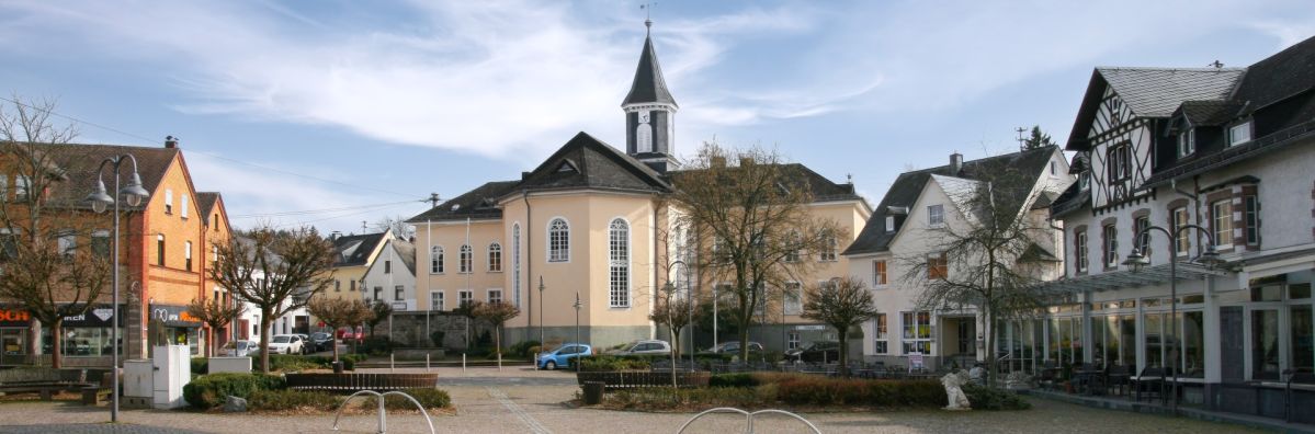 Marktplatz in Selters Marktplatz in Selters mit bepflanzten Grünflächen, umgebenden Wohn- und Geschäftshäusern sowie einer Kirche mit Dachreiter im Zentrum der Stadt.