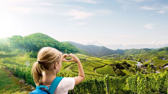 Ein Mädchen formt mit ihren Händen ein Herz und steht in einer grünen, bergigen Umgebung.